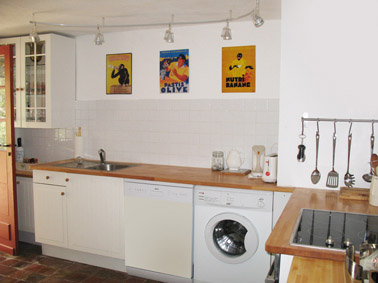 Kitchen with white units and solid beech work surfaces, halogen hob. There nostalgic tin advertising plaques on the wall featuring Banan, Pastis and Choky. 